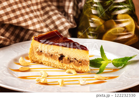 Piece of cheesecake with chocolate and cashew nuts served on a plate at decorated background. Piece of cheesecake with chocolate and cashew nuts served on a plate at decorated background. 122232330