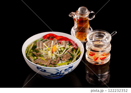 Bowl of vietnamese traditional soup pho with beef meat served with sauces isolated at black background. Bowl of vietnamese traditional soup pho with beef meat served with sauces isolated at black background. 122232352