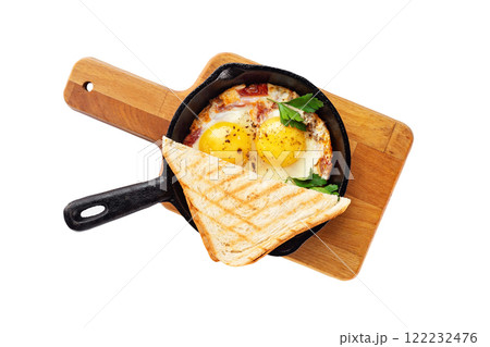 Top view image of fried eggs served in an iron pan at wooden board with bread toasts isolated at white background. Top view image of fried eggs served in an iron pan at wooden board with bread toasts isolated at white background. 122232476