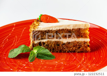 Closeup piece of honey layered cake with cream cheese decorated with mint on a red plate isolated at white background. 122232511