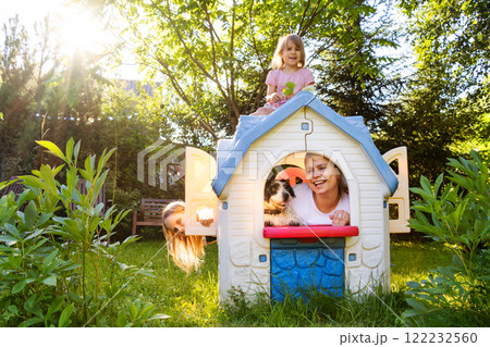 Family playing in a toy house with their dog in a sunny backyard Family playing in a toy house with their dog in a sunny backyard 122232560