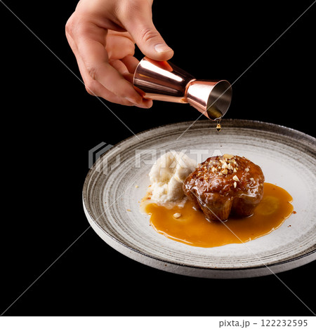 Closeup square image of plate with sweet muffin cake and icecream isolated at black background with copyspace. Male hand with jigger pouring caramel and decorating the pastry. 122232595