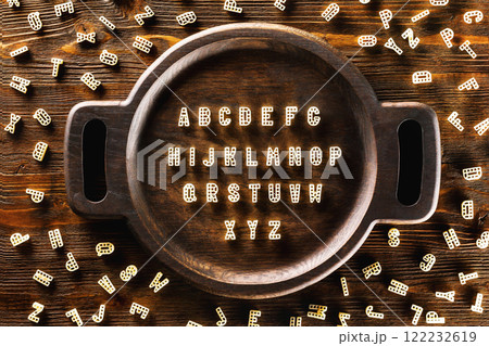 ABC alphabet made of macaroni on round tray at wooden background. 122232619