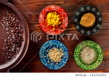 Closeup image of colorful ethnic style plates with spices at wooden table background. 122232622