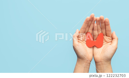 World Thyroid Day concept. Human hand holding thyroid gland shape made from paper on blue background. Awareness of thyroid disease such as hyperthyroidism, hypothyroidism and thyroiditis. World Thyroid Day concept. Human hand holding thyroid gland shape made from paper on blue background. Awareness of thyroid disease such as hyperthyroidism, hypothyroidism and thyroiditis. 122232703
