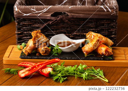 Assortment of asian spring rolls with fresh vegetables and sauce at wooden board at decorated restaurant table background. Assortment of asian spring rolls with fresh vegetables and sauce at wooden board at decorated restaurant table background. 122232736