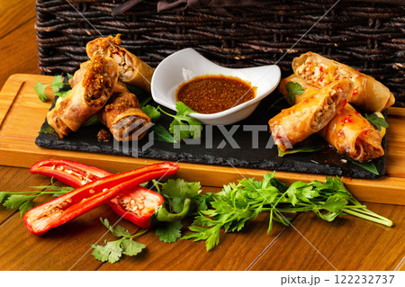 Assortment of asian spring rolls with fresh vegetables and sauce at wooden board at decorated restaurant table background. 122232737