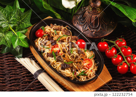 Iron pan of fried egg noodles with beef, tomato and thai sauce at decorated restaurant table background. Iron pan of fried egg noodles with beef, tomato and thai sauce at decorated restaurant table background. 122232754