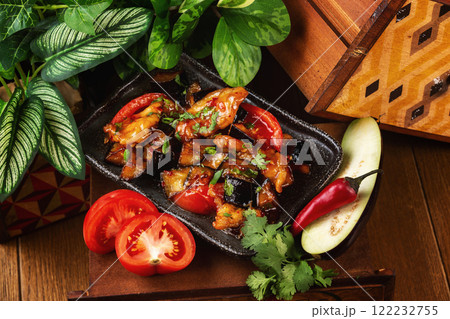 Plate of asian meal - chicken roasted with vegetables and eggplant served with chopsticks at decorated wooden table background. Plate of asian meal - chicken roasted with vegetables and eggplant served with chopsticks at decorated wooden table background. 122232755