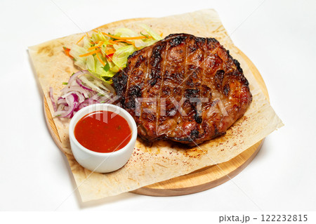 Roasted beef meat steak with sauce at a wooden board served with paper isolated at white background. Roasted beef meat steak with sauce at a wooden board served with paper isolated at white background. 122232815