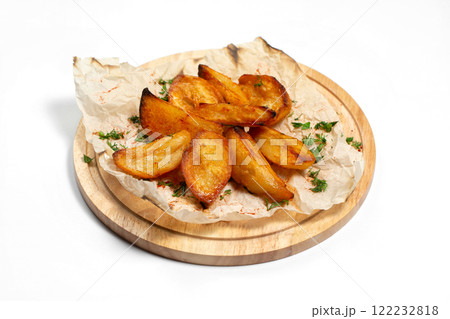 Fried potato wedges on a wooden tray board with paper isolated at white background. Fried potato wedges on a wooden tray board with paper isolated at white background. 122232818