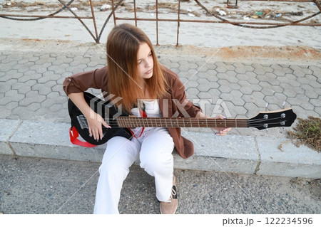 Girl Plays The Bass Instrument Sitting On The Step Near The Street At Evening Girl Plays The Bass Instrument Sitting On The Step Near The Street At Evening 122234596