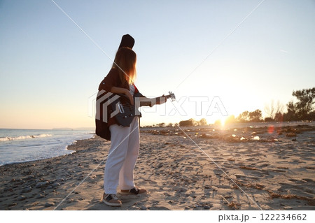 Girl Walks And Plays The Bass Instrument On The Beach Near The Ocean At Sunset Girl Walks And Plays The Bass Instrument On The Beach Near The Ocean At Sunset 122234662