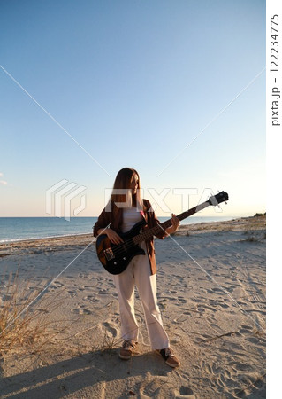 Girl Plays Bass Music Instrument On The Beach At Sunset Near Ocean Girl Plays Bass Music Instrument On The Beach At Sunset Near Ocean 122234775