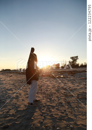 Girl Walks And Plays The Bass Instrument On The Beach Near The Ocean At Sunset Girl Walks And Plays The Bass Instrument On The Beach Near The Ocean At Sunset 122234795