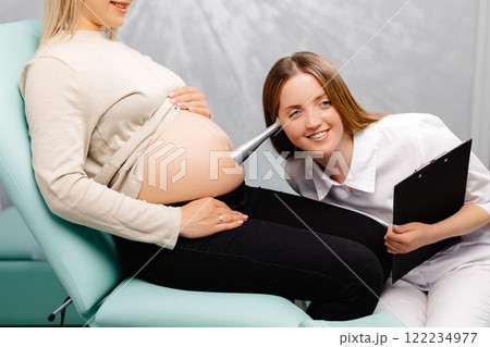 A gynecologist leans a stethoscope to a pregnant woman's belly and listens to the baby's heartbeat A gynecologist leans a stethoscope to a pregnant woman's belly and listens to the baby's heartbeat 122234977