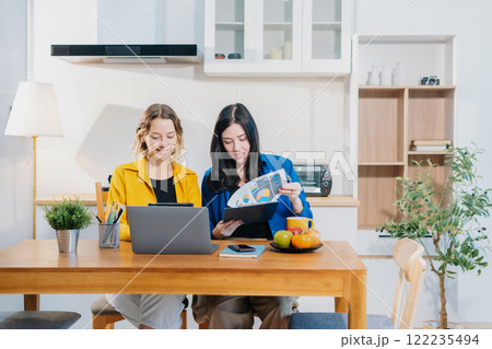 Two Woman sitting in the kitchen at home office reviewing and discussing a business project. Two Woman sitting in the kitchen at home office reviewing and discussing a business project. 122235494