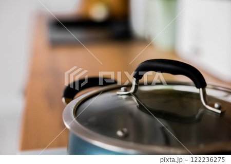 Close-up in focus: a blue saucepan with a transparent lid on which rubber pads on the handles against the background of a wooden kitchen are out of focus. High quality photo Close-up in focus: a blue saucepan with a transparent lid on which rubber pads on the handles against the background of a wooden kitchen are out of focus. High quality photo 122236275