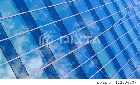 An architectural photograph showcasing curved lines and reflective glass, creating an impression of motion. The mirror-like windows capture clouds in their reflection, blending natural and constructed 122236387