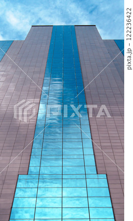 Modern Grandeur. A Vertical Perspective of a Glass and Metal Skyscraper, Reflecting the Clear Blue Sky and Achieving Architectural Elegance Through Symmetry and Clean Lines. 122236422