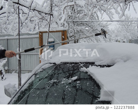 hand with long scraper removing snow from roof of car in private yard after heavy snowfall, clearing car manually after snow storm, driver removing layer of snow from grey car with long handled device hand with long scraper removing snow from roof of car in private yard after heavy snowfall, clearing car manually after snow storm, driver removing layer of snow from grey car with long handled device 122237888
