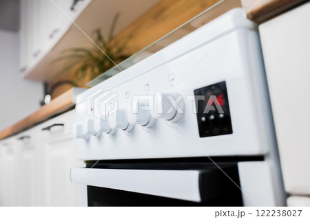Close-up in focus panel with rotary control knobs at kitchen white gas stove against wooden countertop background and white cabinets of modern kitchen out of focus. Concept of cooking, temperature Close-up in focus panel with rotary control knobs at kitchen white gas stove against wooden countertop background and white cabinets of modern kitchen out of focus. Concept of cooking, temperature 122238027