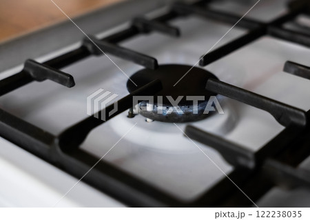 Close-up of a white gas stove with a black cast-iron grate and a black burner on which a blue fire burns. Gas stove, cooking concept. High quality photo 122238035