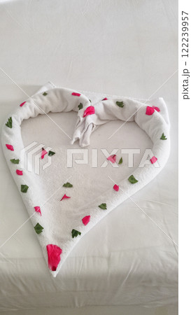Heart shaped towel decorated with flower petals lying on hotel bed Valentines day at sataya resort Valentines day Heart shaped towel decorated with flower petals lying on hotel bed Valentines day at sataya resort Valentines day 122239957
