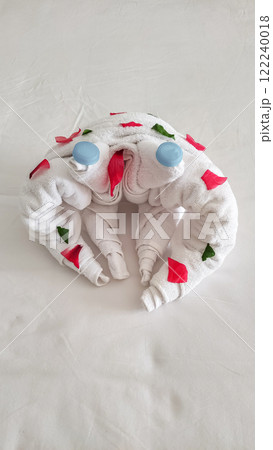 White towel folded as crab decorated with flower petals lying on bed in hotel room Valentines day 122240018