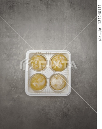 Four mango mochi resting in plastic container on marble countertop 122240133