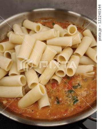 Rigatoni pasta added to tomato sauce in stainless steel pan Rigatoni pasta added to tomato sauce in stainless steel pan 122240144