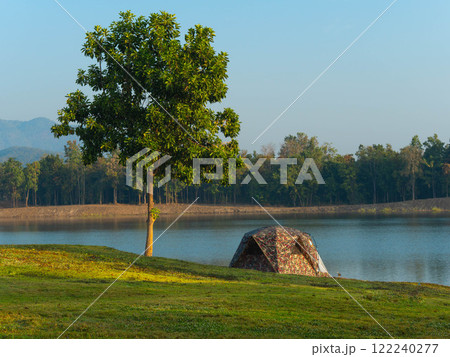 Towering trees by the lake and tents at a beautiful sunrise. 122240277