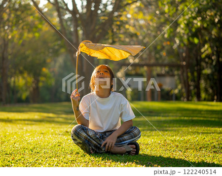Happy little girl outdoors in nature and having fun picking leaves with beautiful warm sunset in the park. 122240514