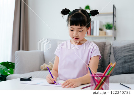 A cute little girl is drawing and coloring with colored pencil on a piece of paper 122240782