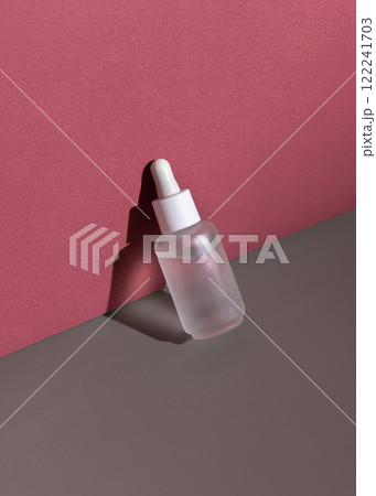 Clear glass dropper bottle on grey and red background with hard shadow closeup, cosmetic mockup 122241703