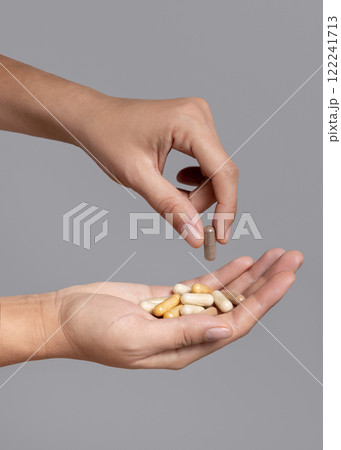 Female hand taking one beige medical capsule and holding others in cupped hand against grey 122241713