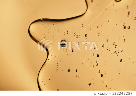 The beautiful texture of the cosmetic serum on a gold background that takes up most of the photo. The beautiful texture of the cosmetic serum on a gold background that takes up most of the photo. 122242287