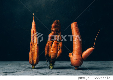 Three carrots are standing on a counter, one of which is bent and twisted 122243612