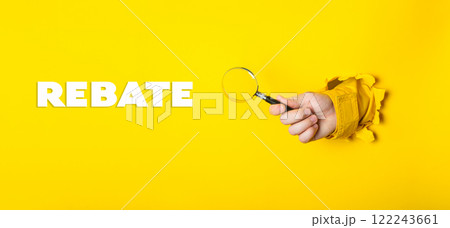 Hand holding a magnifying glass over a yellow background with the word REBATE 122243661