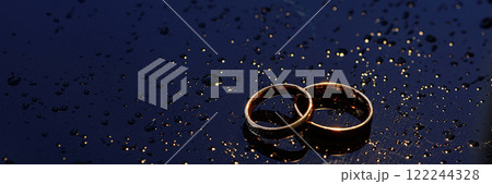 Banner two gold wedding rings lie on a dark wet surface 122244328