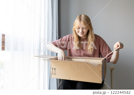 Young cheerful woman in glasses getting parcel at home. Pretty girl sitting on sofa at home and opening carton box. Express delivery service and satisfied consumer. Online shopping banner Young cheerful woman in glasses getting parcel at home. Pretty girl sitting on sofa at home and opening carton box. Express delivery service and satisfied consumer. Online shopping banner 122244582