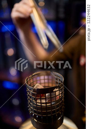 Close up of a hookah made of metal and glass on a wooden table Close up of a hookah made of metal and glass on a wooden table 122244632