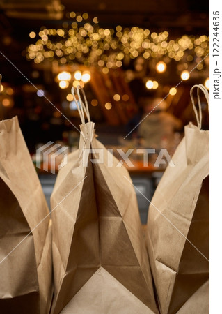 There are three craft paper bags placed neatly on a rustic wooden counter inside a cafe setting There are three craft paper bags placed neatly on a rustic wooden counter inside a cafe setting 122244636