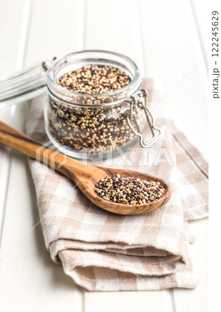 Mixed uncooked quinoa seeds on wooden spoon on white table. 122245629