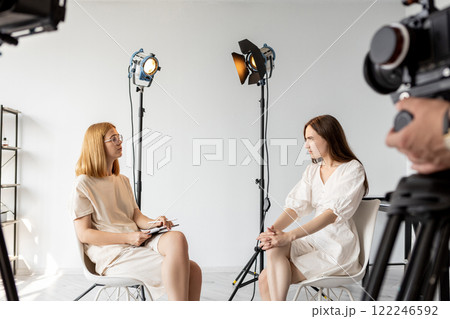 Studio conversation. Producer talk. Art director questions female model near cameras. Backstage video interview preparation photo shoot. Studio conversation. Producer talk. Art director questions female model near cameras. Backstage video interview preparation photo shoot. 122246592
