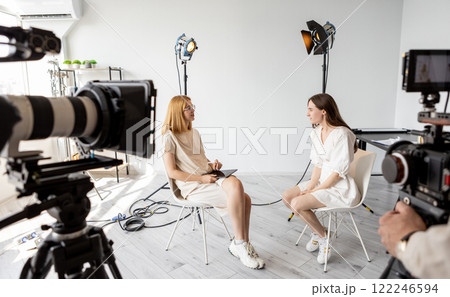 Dialogue project. Backstage studio. Video recording business conversation between two women. Female models sit on chairs pose photo shoot. Dialogue project. Backstage studio. Video recording business conversation between two women. Female models sit on chairs pose photo shoot. 122246594