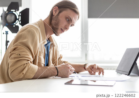 Script writing. Paper work. Guy taking notes documents in photo studio adjusts sign shooting advertising production at workplace. Script writing. Paper work. Guy taking notes documents in photo studio adjusts sign shooting advertising production at workplace. 122246602