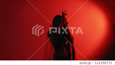 Female dance. Movement therapy. Relaxed woman silhouette in trance wearing polyethylene rags performing graceful hand activity isolated on dark red glow copy space background. 122246772