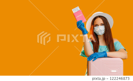 Pandemic trip. Summer vacation. Tourist woman in protective mask gloves with passport tickets suitcase waiting for flight check-in isolated on orange empty space background. Pandemic trip. Summer vacation. Tourist woman in protective mask gloves with passport tickets suitcase waiting for flight check-in isolated on orange empty space background. 122246873