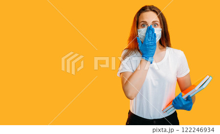 Pandemic shock. Social distancing. Scared female student in protective face mask gloves isolated on yellow color copy space background. Pandemic shock. Social distancing. Scared female student in protective face mask gloves isolated on yellow color copy space background. 122246934